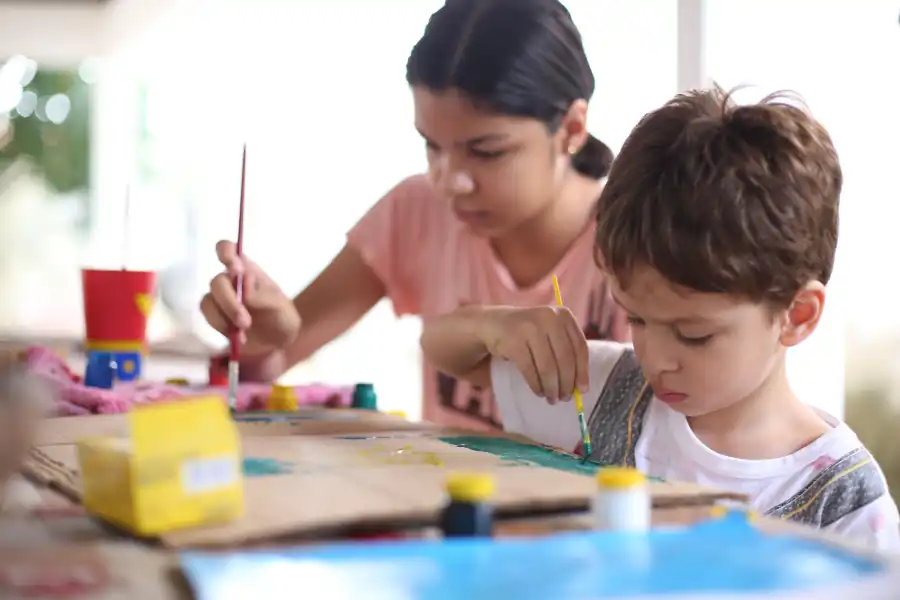 Adolescente e criança pintando juntos numa mesa de trabalho
