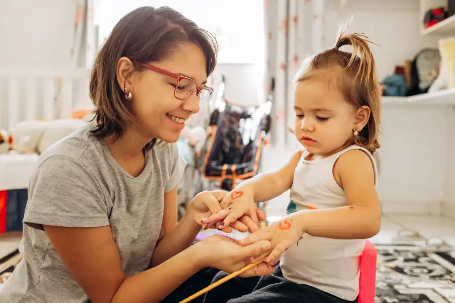 Educadora e criança pequena sentadas no chão, brincando juntas