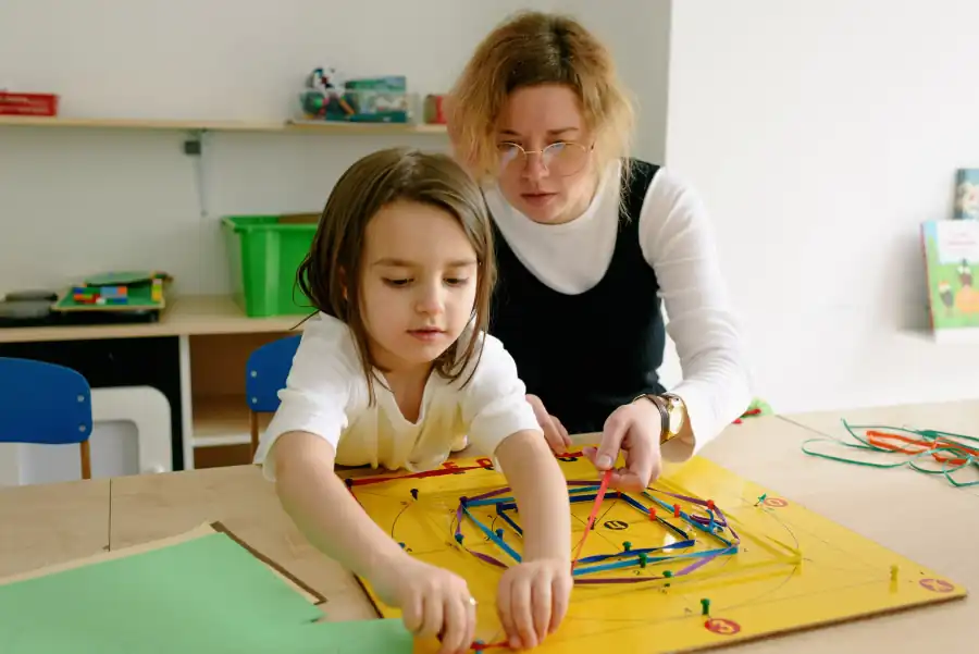 Menina e professora trabalhando com material pedagógico colorido sobre a mesa
