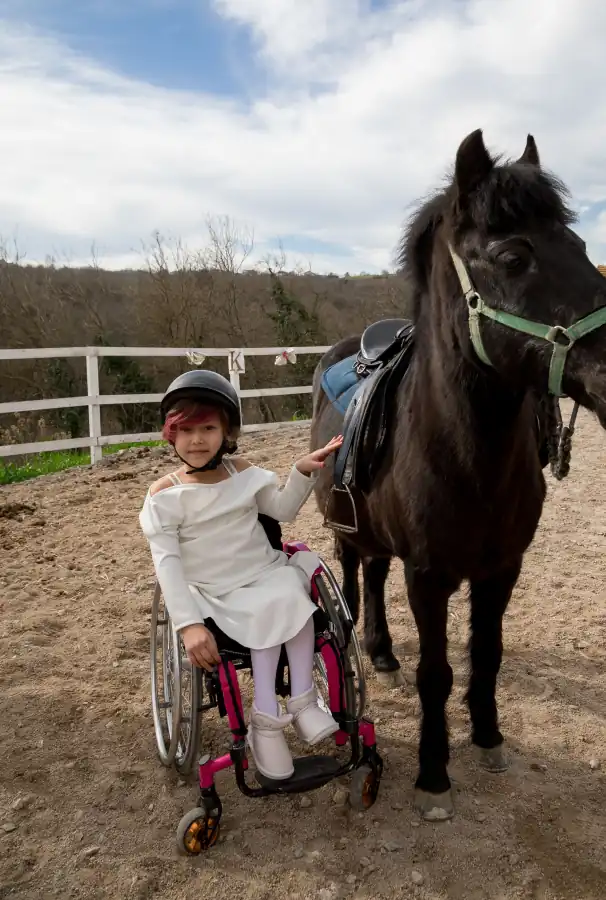 Criança em cadeira de rodas ao lado de um cavalo, na sessão de equoterapia