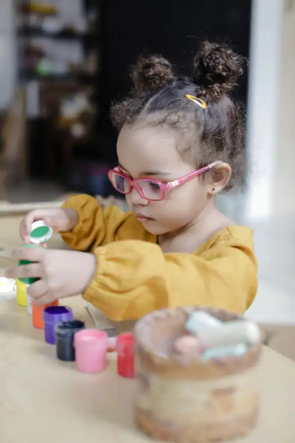 Criança pequena manipulando potes coloridos sobre a mesa